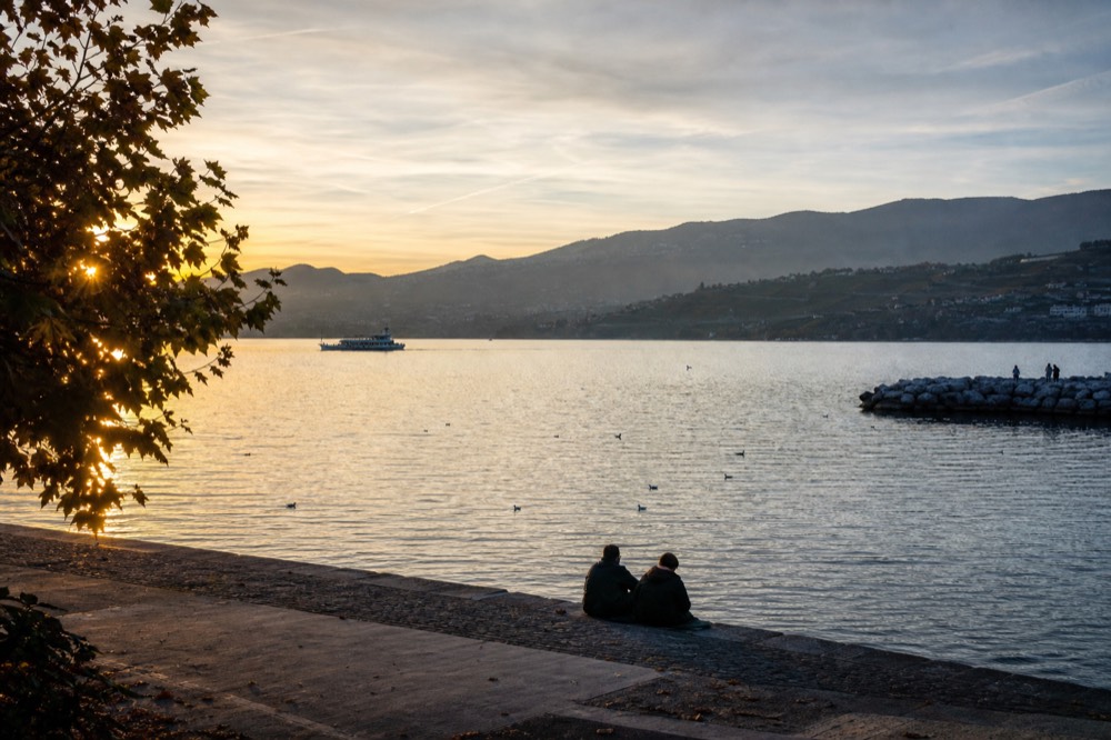Lake Geneva at golden hour near Lausanne-Ouchy in autumn, low sun over the vineyard terraces and calm water
