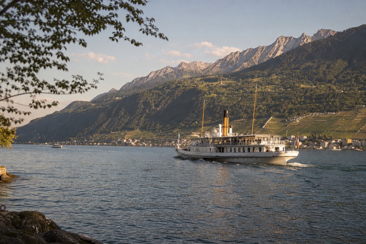 A CGN cruise boat on Lake Geneva off Montreux in golden-hour light, the Alps across the water and Lavaux vineyard slopes on the Swiss shore