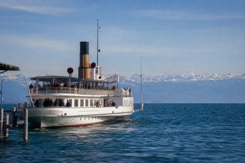 A CGN scheduled boat leaving Lausanne-Ouchy on Lake Geneva, passengers on deck and the Alps across the water