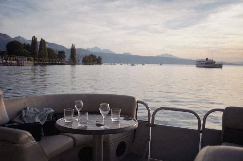 An open pontoon boat on Lake Geneva at golden hour off Geneva, glasses set out on the deck and the shoreline behind