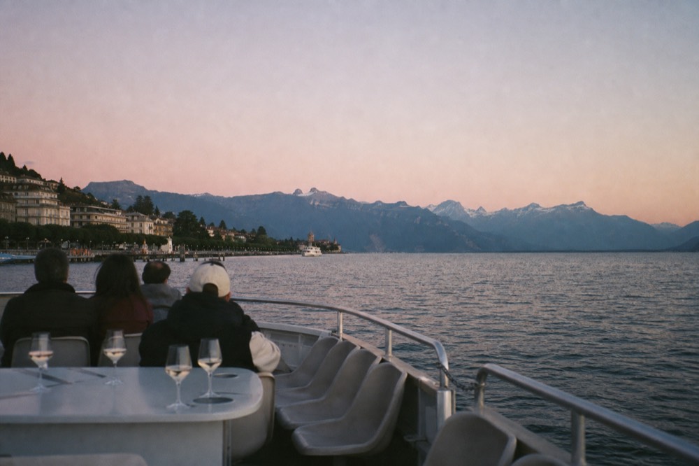 An open pontoon boat on Lake Geneva at golden hour, glasses set out on the deck and the Geneva shoreline behind