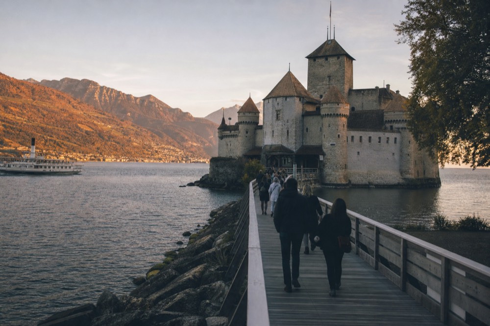 Visitors crossing the wooden bridge to the entrance of Château de Chillon near Montreux, the castle towers rising from the lake