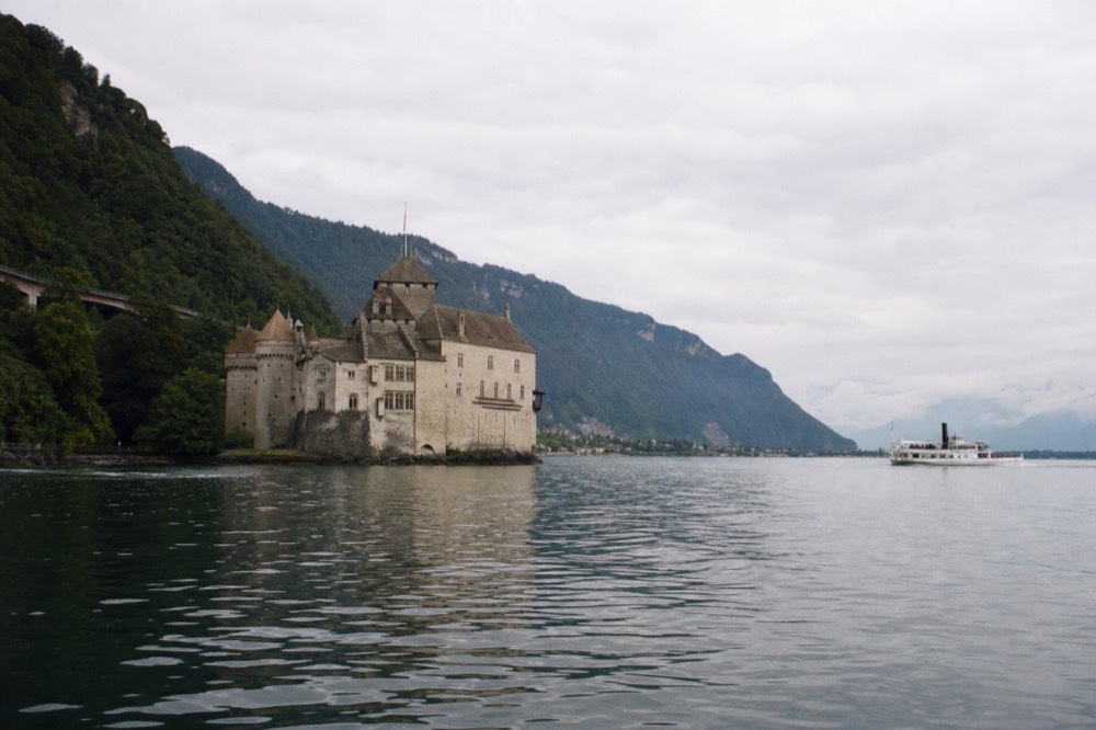 The Château de Chillon on its rock beside Lac Léman near Montreux, seen from the water with wooded hills behind