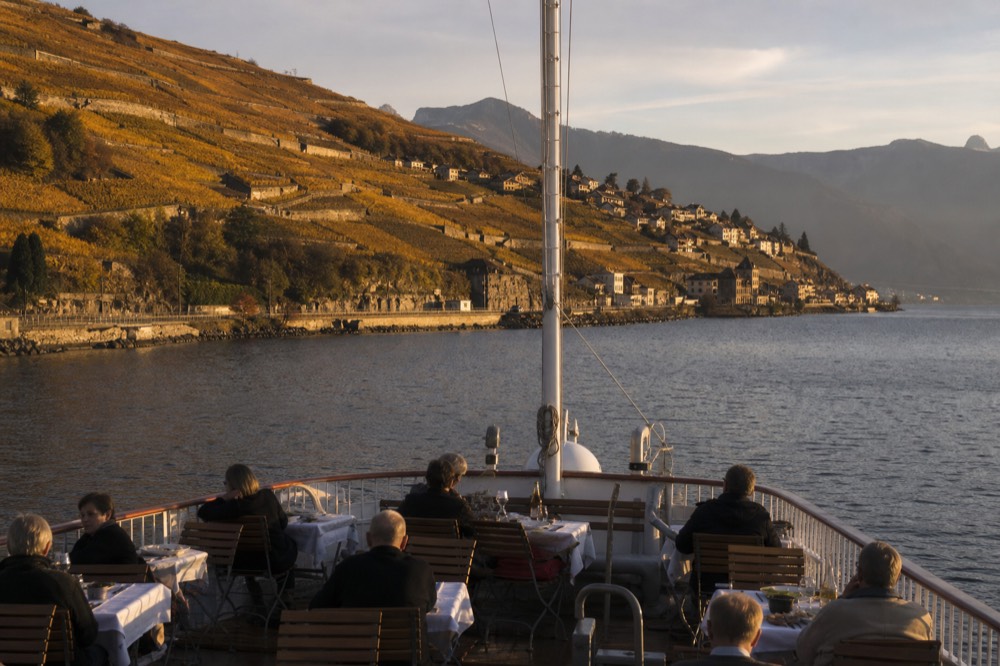 A CGN cruise boat passing the Lavaux vineyard terraces near Vevey at midday, the open deck set for lunch