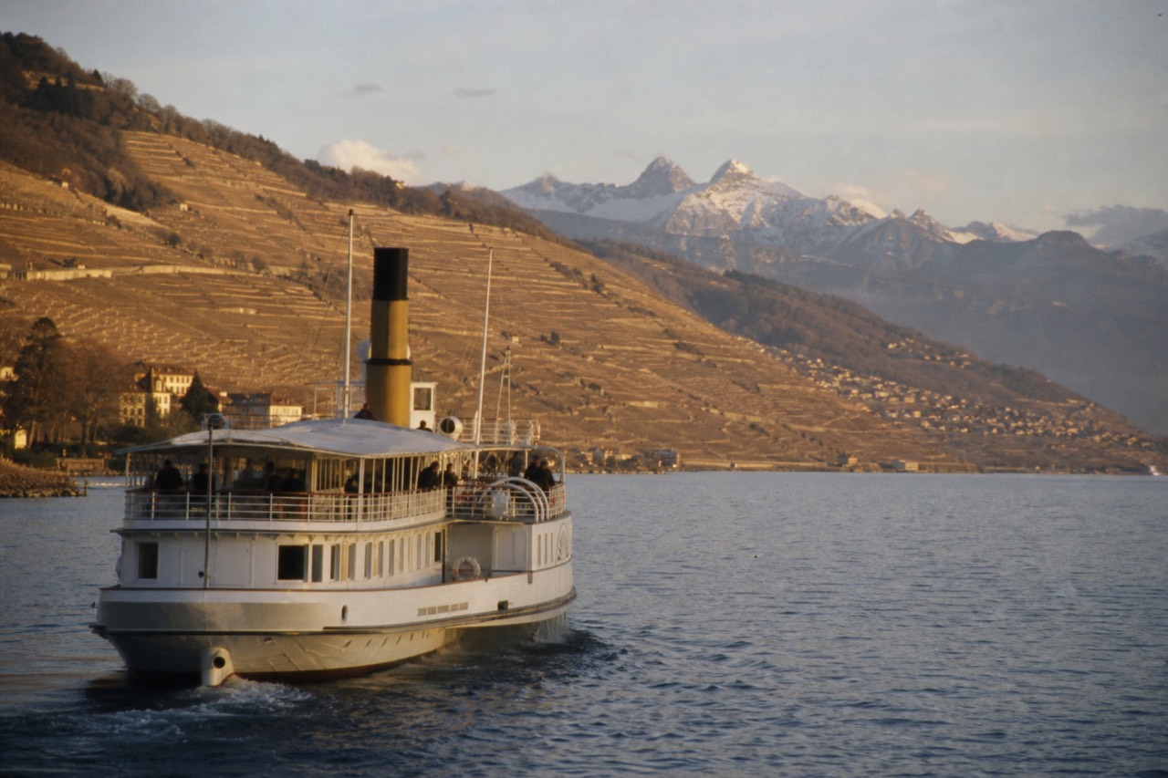 A plain-hulled CGN passenger ferry crossing Lake Geneva from Lausanne-Ouchy toward the French shore, the Alps across the water