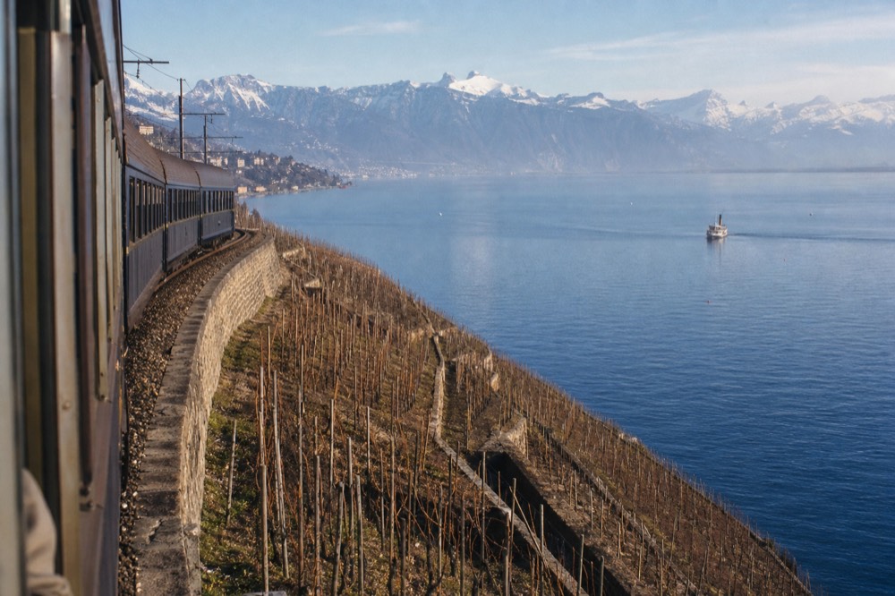 A train running along the lakeside through the Lavaux vineyard terraces near Vevey on Lake Geneva, the water and Alps below the track
