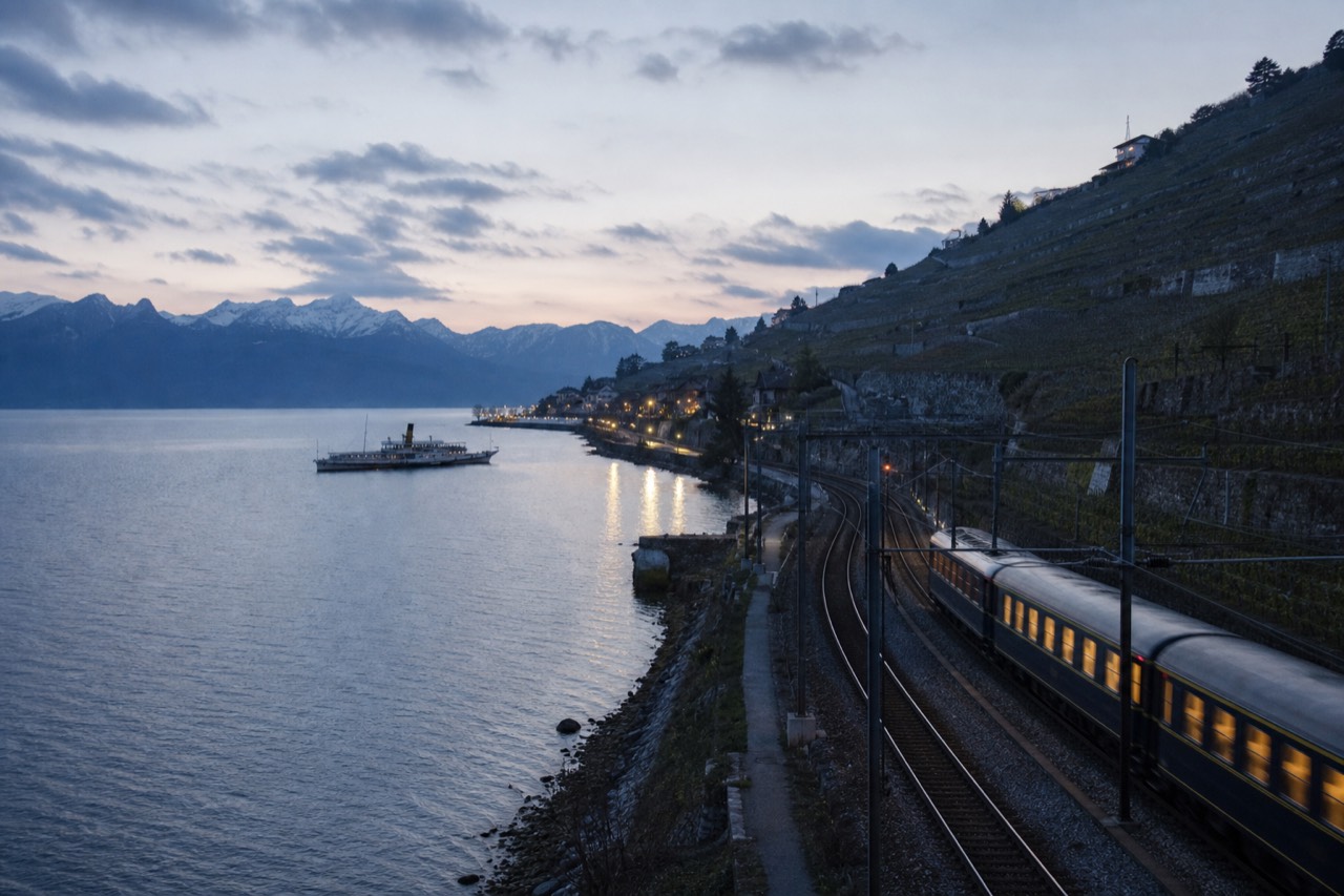 A lakeside railway running along the shore of Lake Geneva near Lausanne in Switzerland, vineyard terraces above the track and the Alps across the water
