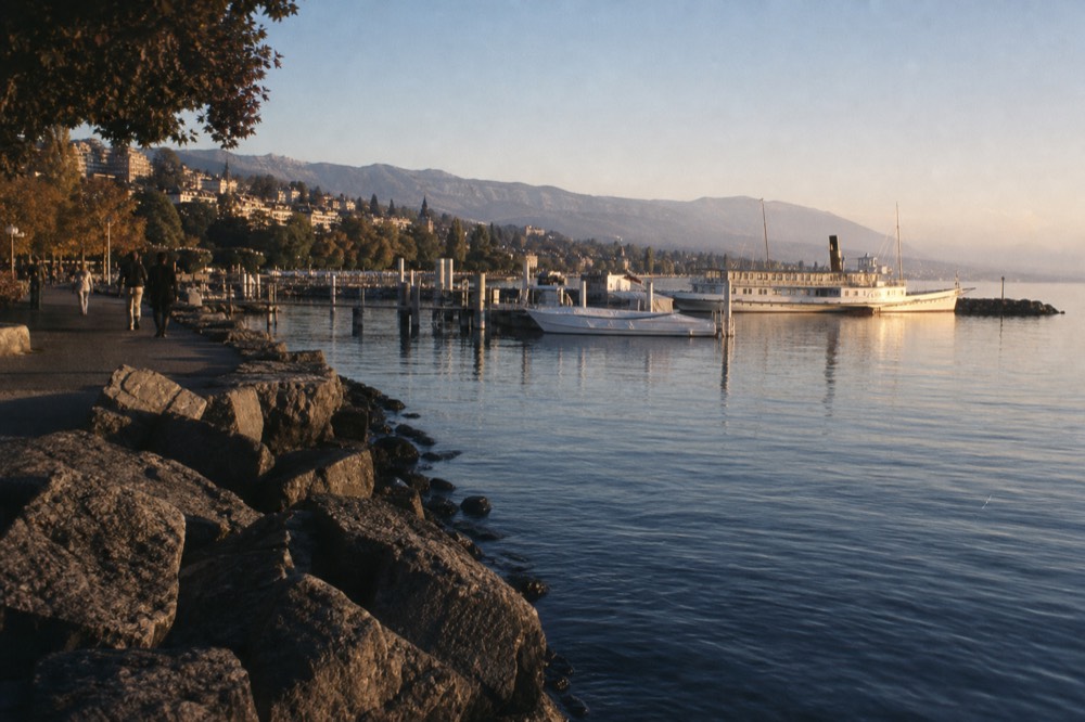 The Ouchy waterfront at Lausanne on Lac Léman, a lakeside promenade with boats at the pier and hills behind