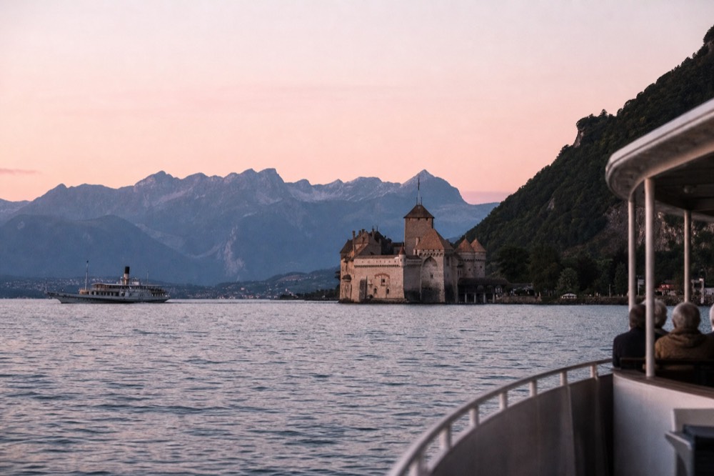 The Château de Chillon on its rock at Veytaux seen from a boat on Lake Geneva near Montreux, the Alps behind
