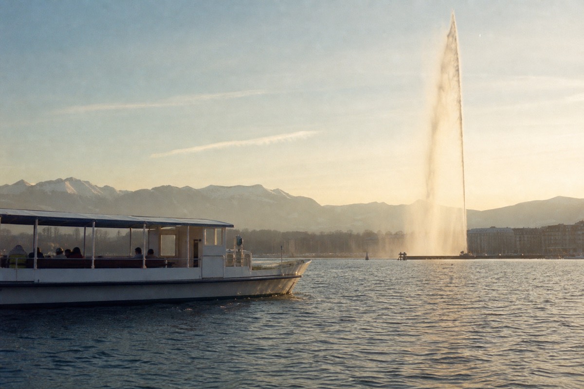 A cruise boat on Lake Geneva off the Geneva shore, the Jet d'Eau rising from the water and the Alps in the distance