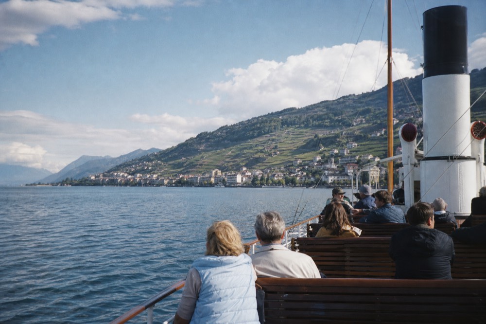 Passengers on the open deck of a Belle Époque paddle steamer on Lac Léman, the Riviera shoreline behind