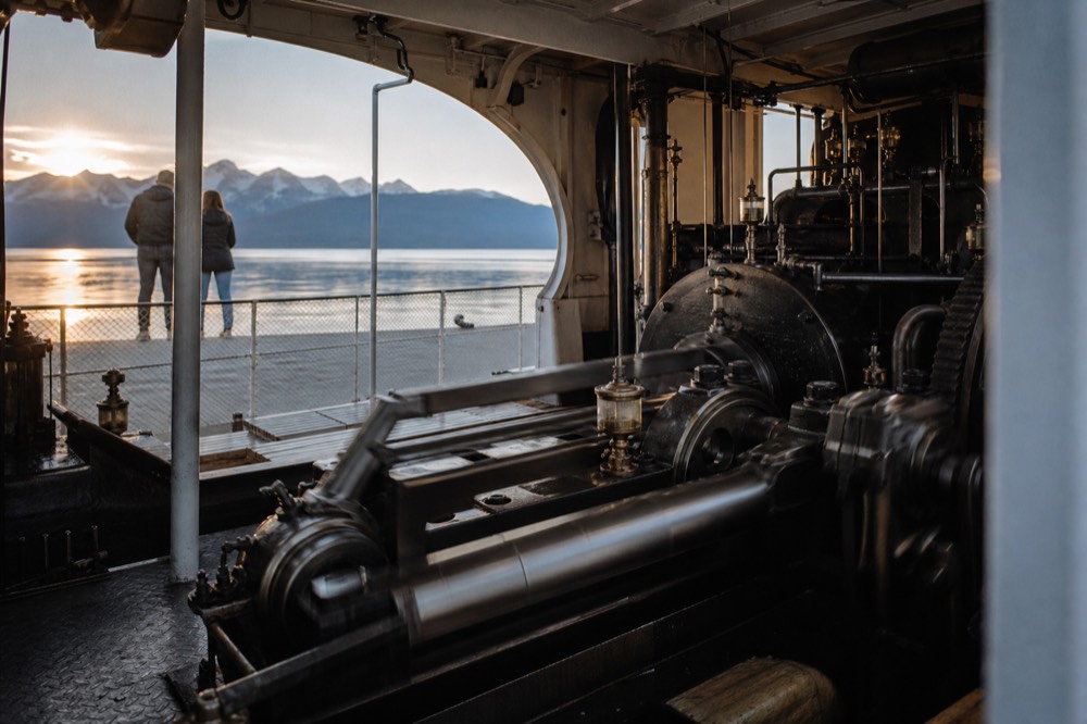 The open steam engine room of a Belle Époque paddle boat on Lac Léman, polished pistons driving the paddle shaft