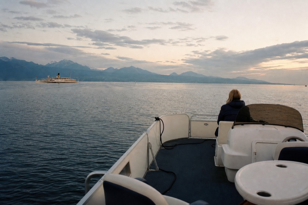 A small open pontoon boat on Lake Geneva off the Geneva lakefront at golden hour, the Alps across the water