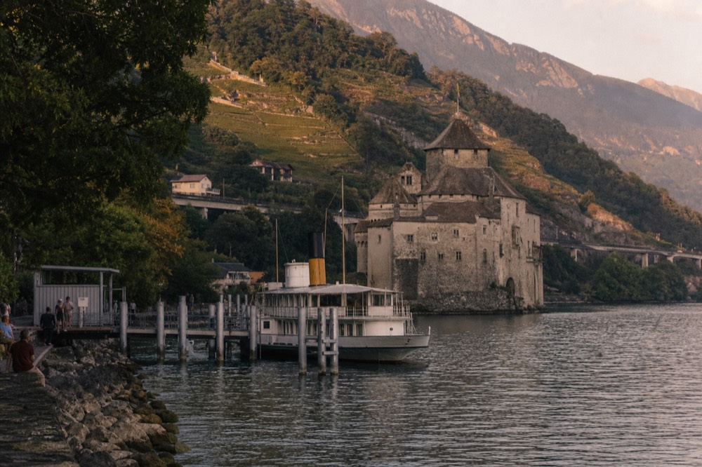 A cruise boat at the Chillon landing stage on Lake Geneva at Veytaux, Château de Chillon rising from the shore beside it