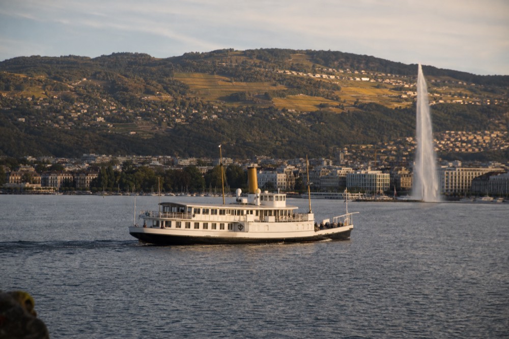 A small CGN cruise boat crossing the Petit Lac off Geneva on Lake Geneva, the harbour and Jet d'Eau behind
