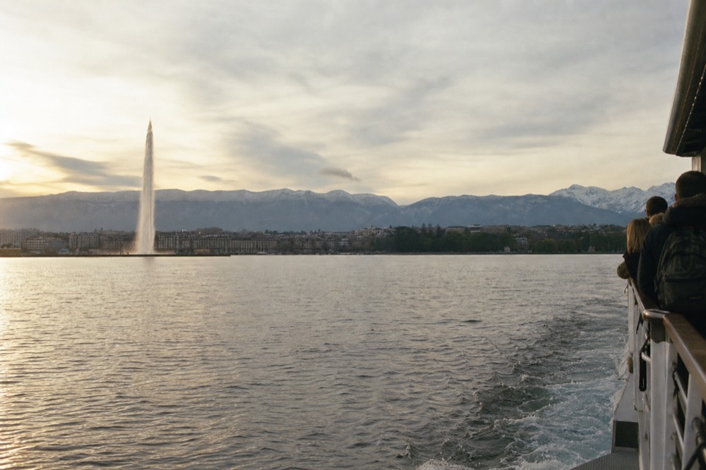 A CGN boat leaving the Geneva lakefront on Lake Geneva at golden hour, the Jet d'Eau and the Alps across the water