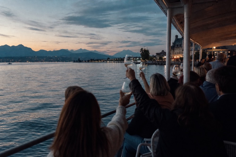 Diners raising glasses on the deck of a cruise boat on Lac Léman, the sun low over the water off Geneva