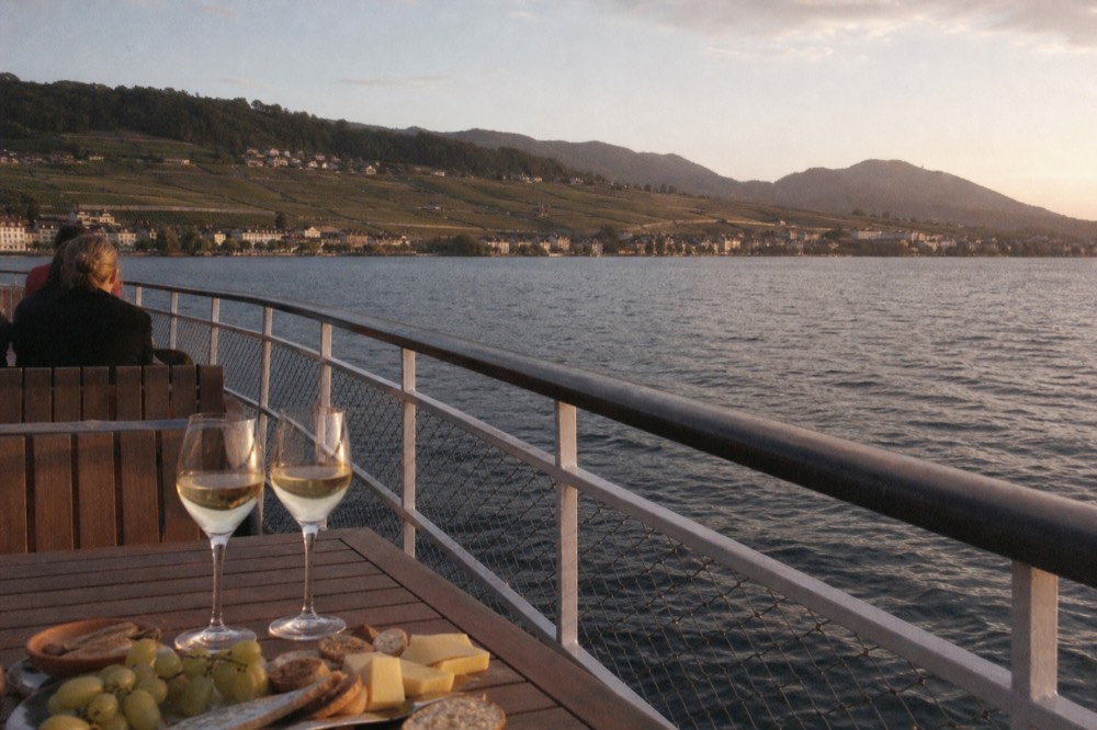 A solar-powered scenic cruise boat on Lac Léman off Geneva, wine and snacks on a deck table in afternoon light