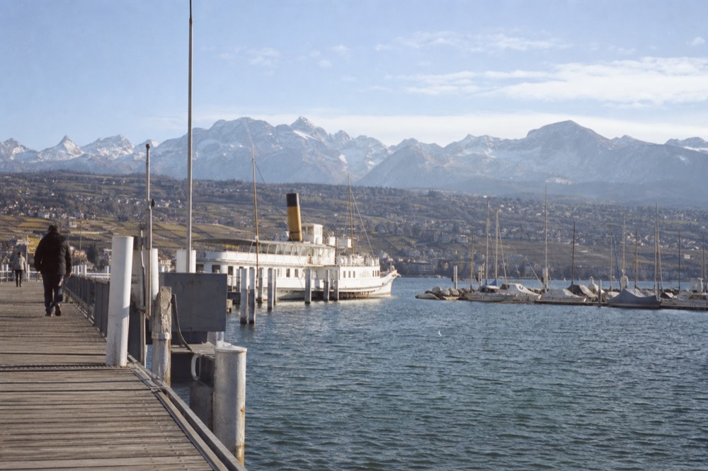 The Genève-Mont-Blanc pier on Lake Geneva, boats moored along the Geneva lakefront with the Alps beyond