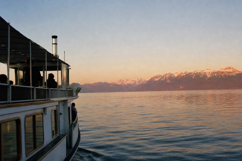 A cruise boat on Lake Geneva off Lausanne-Ouchy at dusk with the Alps across the water