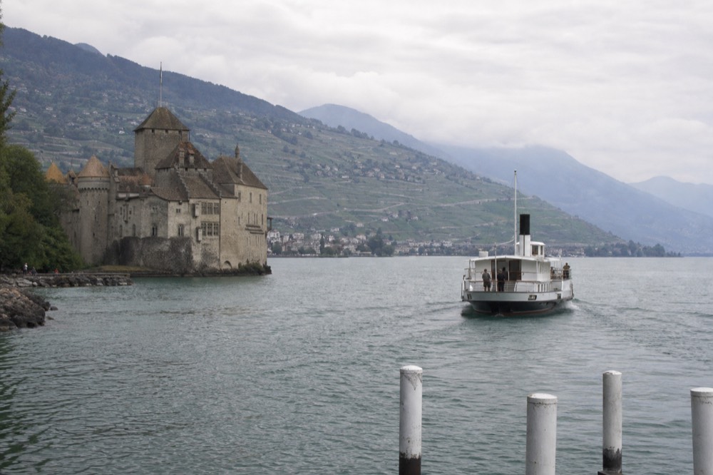 Château de Chillon on the shore of Lac Léman with the Lavaux and Riviera hills behind, a boat approaching the landing stage