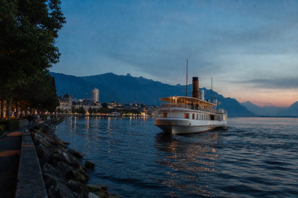 A cruise boat leaving Montreux on Lake Geneva, the Riviera promenade and the mountains behind