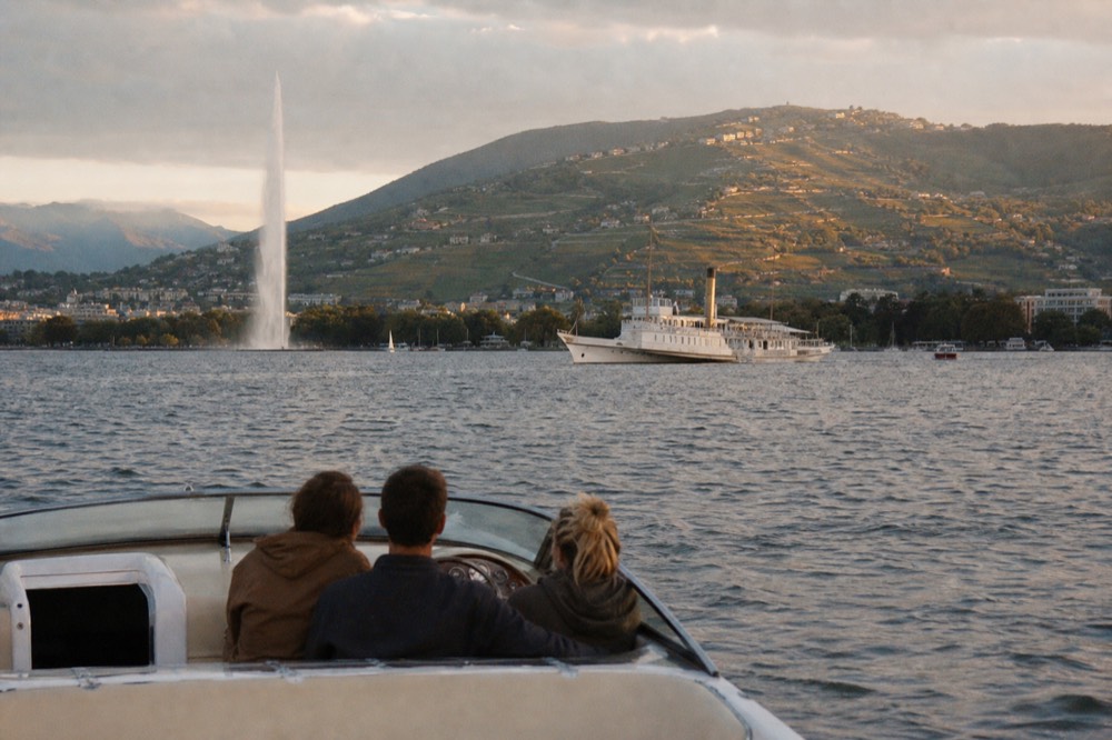 A small open private boat with a few people aboard on the Petit Lac off Geneva, the Jet d'Eau in the background