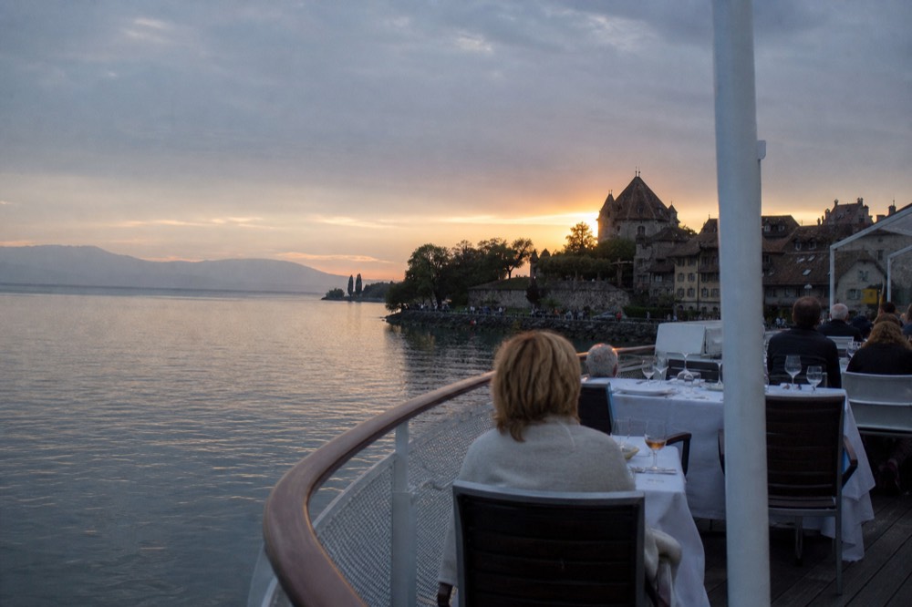 A gourmet dinner served on a boat deck on Lac Léman at sunset, the shoreline of Yvoire in the last light