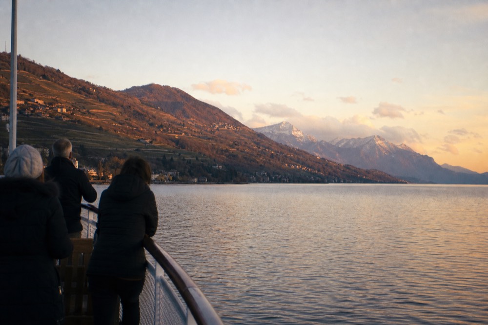 People watching the sunset from the deck of a cruise boat on Lac Léman, the Alps glowing across the water off the Riviera