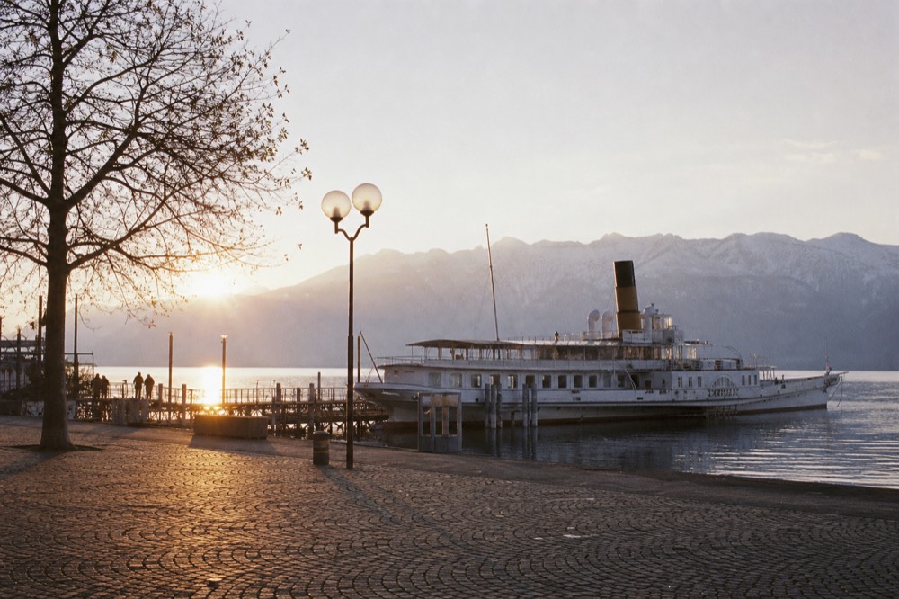 The Vevey lakefront square on Lake Geneva with a cruise boat at the quay and the Alps across the water